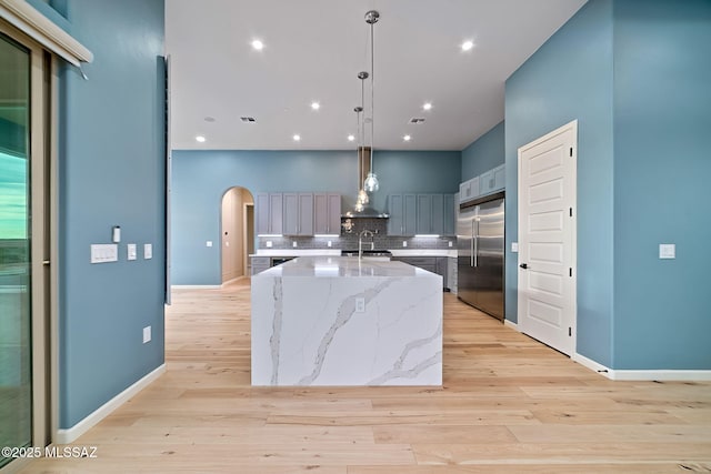 kitchen with sink, stainless steel built in refrigerator, a spacious island, light stone countertops, and tasteful backsplash