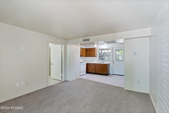 unfurnished living room with light carpet, brick wall, and sink