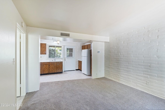 unfurnished living room featuring brick wall, light colored carpet, and sink