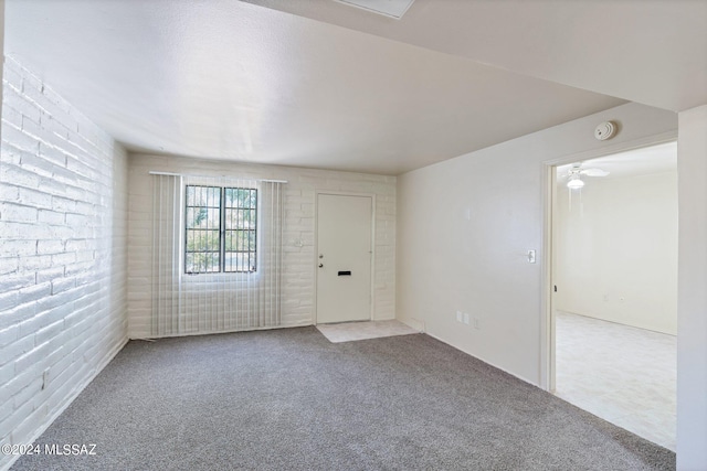 spare room featuring light colored carpet and brick wall