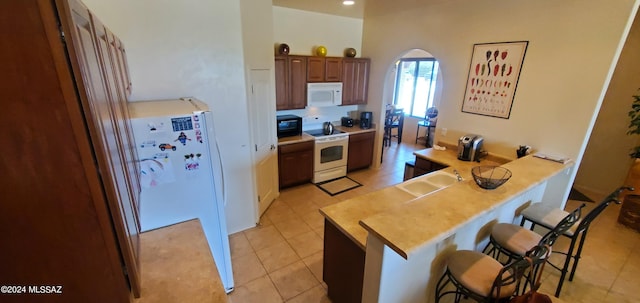 kitchen featuring light tile patterned floors, sink, kitchen peninsula, white appliances, and a kitchen bar