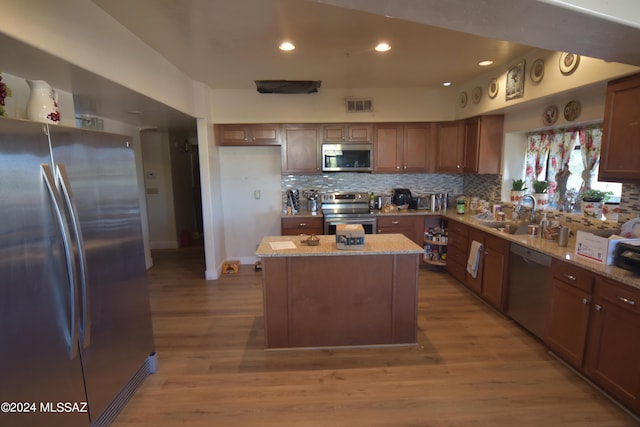 kitchen featuring appliances with stainless steel finishes, light stone countertops, wood-type flooring, a center island, and sink