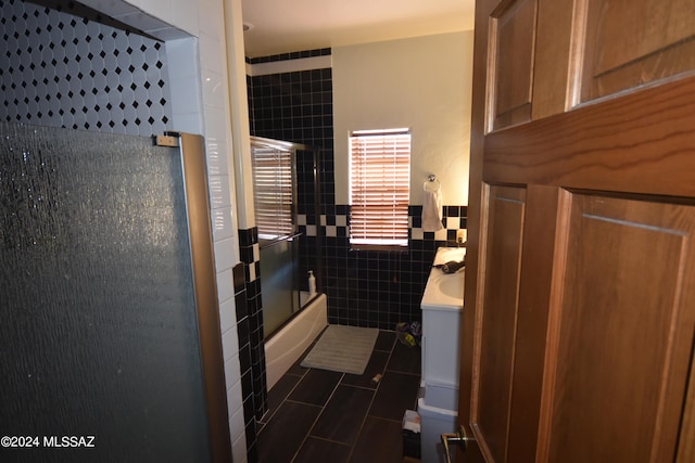 bathroom with tile walls, tile patterned floors, vanity, and bath / shower combo with glass door