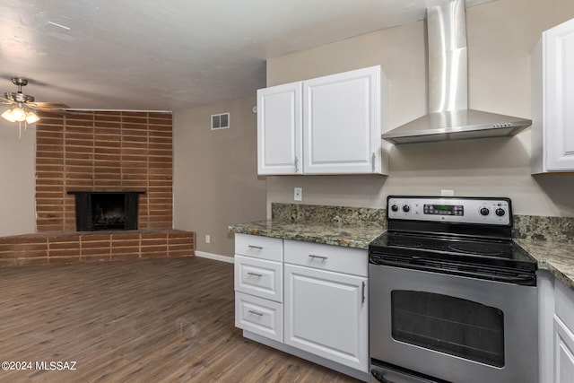 kitchen featuring wall chimney range hood, wood-type flooring, stainless steel electric stove, white cabinets, and dark stone countertops