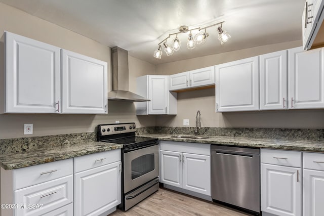 kitchen featuring white cabinets, appliances with stainless steel finishes, light wood-type flooring, wall chimney exhaust hood, and sink