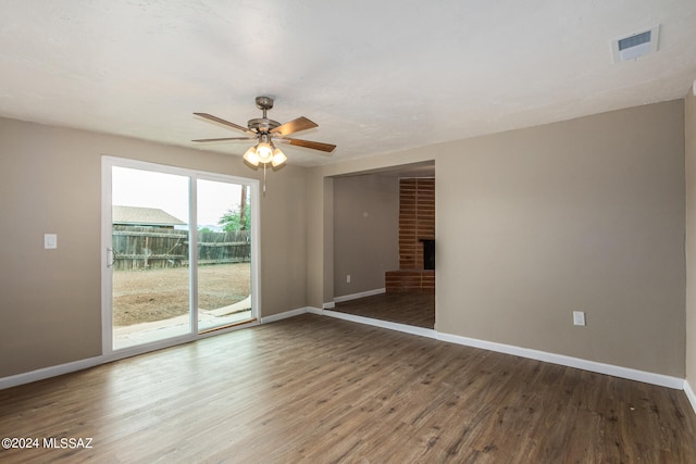 spare room with ceiling fan, dark wood-type flooring, and a brick fireplace