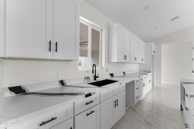 kitchen with light stone countertops, white cabinetry, sink, and lofted ceiling