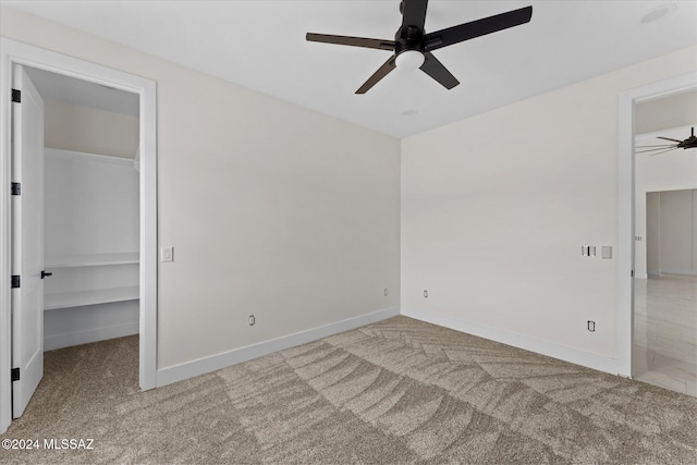 unfurnished bedroom featuring ceiling fan, light carpet, a closet, and a walk in closet