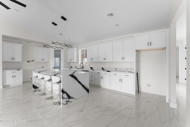 kitchen featuring light stone countertops, decorative light fixtures, lofted ceiling, a center island, and white cabinets