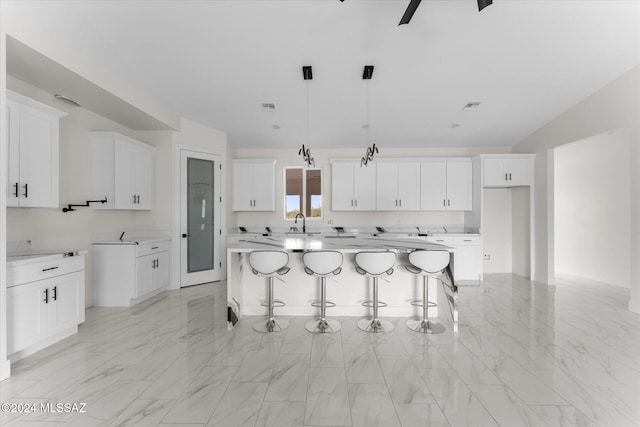 kitchen with pendant lighting, a breakfast bar area, sink, a kitchen island, and white cabinetry