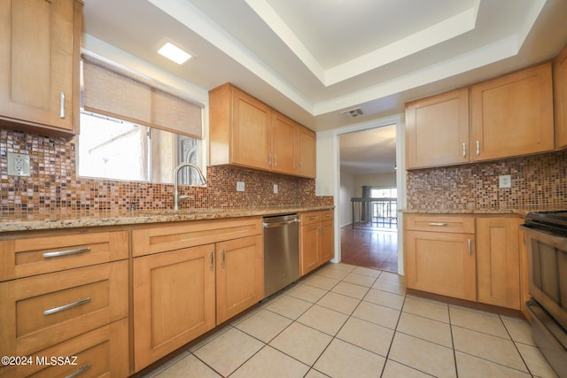 kitchen with backsplash, light stone counters, stainless steel appliances, a tray ceiling, and light tile patterned flooring