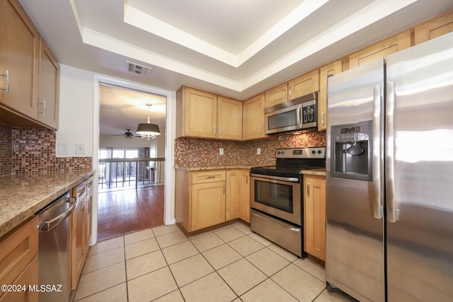 kitchen featuring light tile patterned flooring, stainless steel appliances, light brown cabinetry, and a tray ceiling