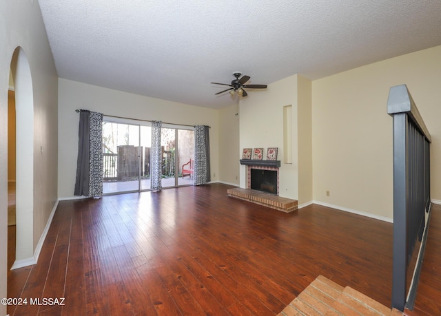 unfurnished living room featuring a fireplace, a textured ceiling, ceiling fan, and dark wood-type flooring