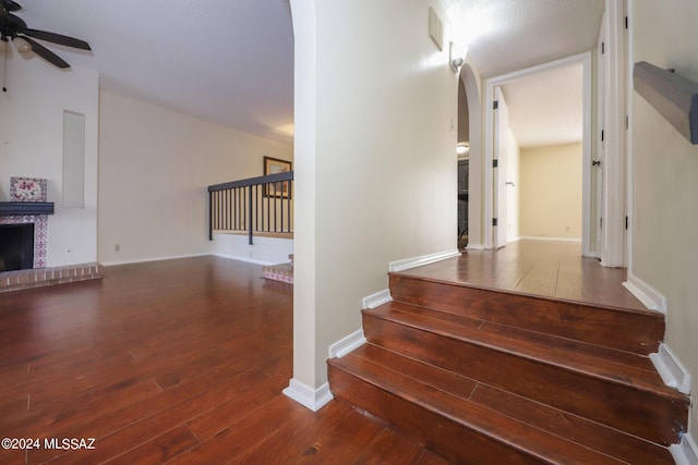 staircase featuring hardwood / wood-style floors, ceiling fan, and a fireplace