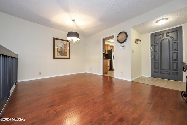 foyer entrance with baseboards, a textured ceiling, and wood finished floors