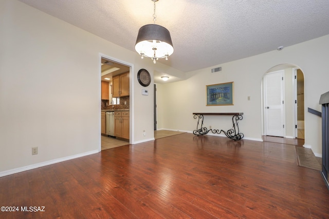 unfurnished living room with arched walkways, baseboards, light wood finished floors, and a textured ceiling