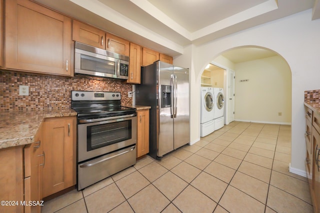 kitchen with decorative backsplash, light stone countertops, light tile patterned floors, appliances with stainless steel finishes, and washing machine and clothes dryer