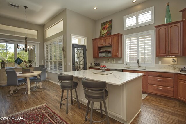 kitchen with dark wood-type flooring, sink, light stone countertops, decorative light fixtures, and a kitchen island