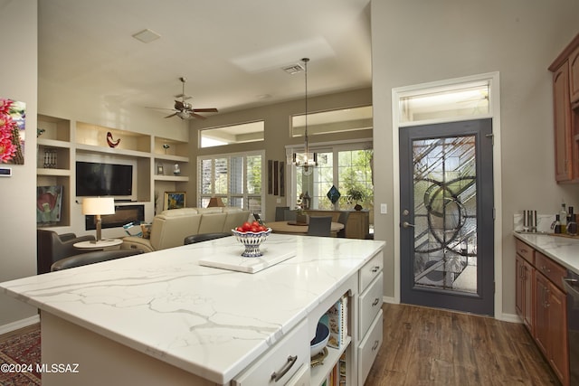 kitchen with dark wood-style flooring, a center island, ceiling fan with notable chandelier, light stone counters, and pendant lighting