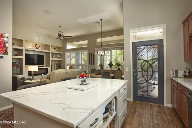 kitchen with hanging light fixtures, light stone counters, dark hardwood / wood-style floors, a kitchen island, and ceiling fan with notable chandelier