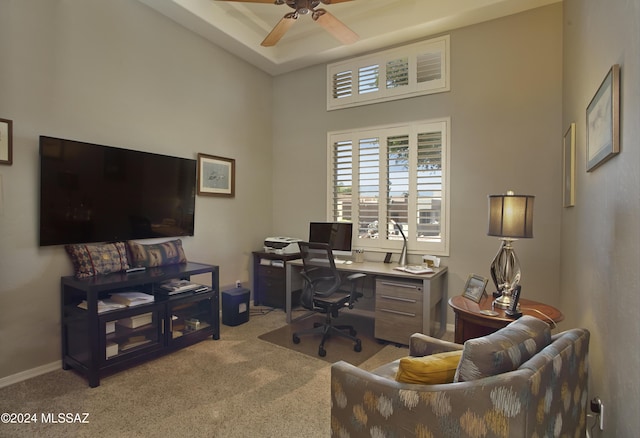 carpeted office space featuring baseboards, ceiling fan, and a raised ceiling
