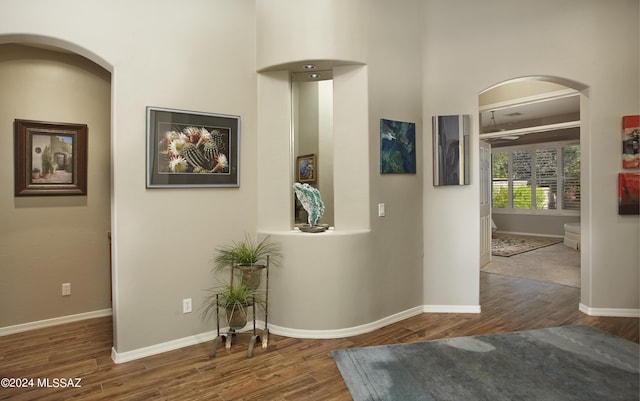 hallway featuring arched walkways, baseboards, and wood finished floors