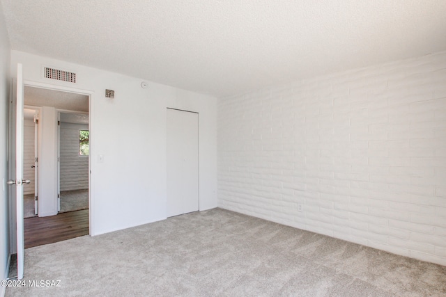 empty room with a textured ceiling, light colored carpet, and brick wall