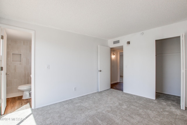 unfurnished bedroom featuring ensuite bath, a closet, light colored carpet, and a textured ceiling