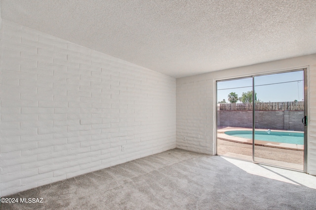 empty room featuring a textured ceiling, light carpet, and brick wall