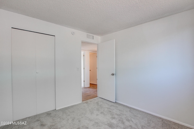 unfurnished bedroom featuring a textured ceiling, light carpet, and a closet