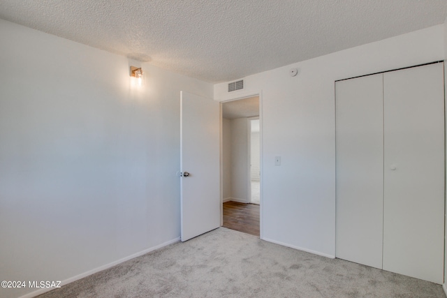 unfurnished bedroom featuring a textured ceiling, light colored carpet, and a closet