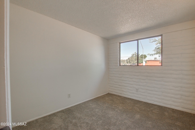 unfurnished room featuring a textured ceiling, brick wall, and carpet flooring