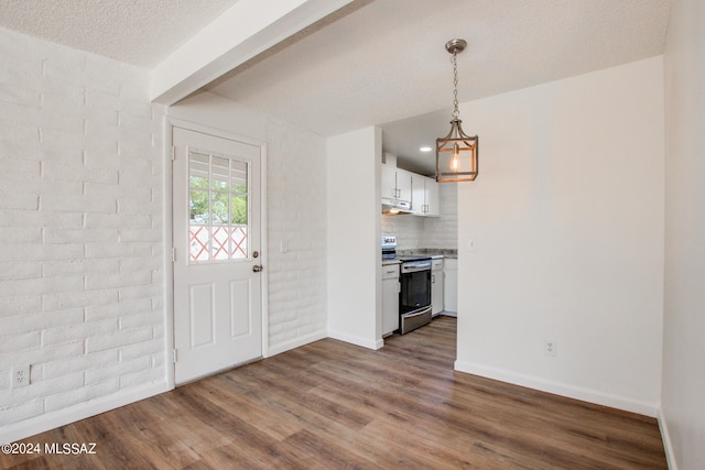 foyer entrance featuring a textured ceiling, dark hardwood / wood-style flooring, a chandelier, and brick wall