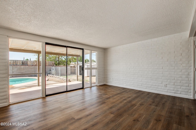 empty room featuring a textured ceiling, wood-type flooring, and brick wall