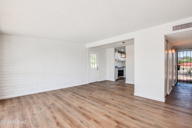 unfurnished living room with brick wall, hardwood / wood-style flooring, and a textured ceiling