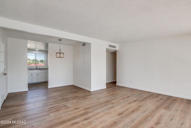 empty room featuring a textured ceiling, light wood-type flooring, and sink