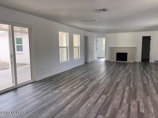 unfurnished living room featuring a fireplace, dark hardwood / wood-style flooring, and a healthy amount of sunlight