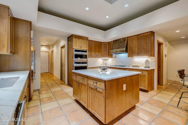 kitchen with tasteful backsplash, a kitchen island, appliances with stainless steel finishes, custom range hood, and light stone countertops