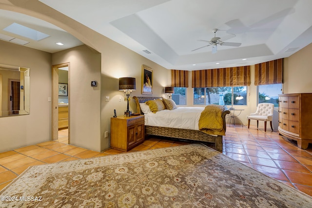 tiled bedroom with a raised ceiling, a skylight, and ceiling fan