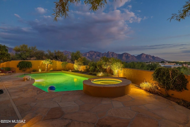 pool at dusk featuring an in ground hot tub, a mountain view, and a patio area