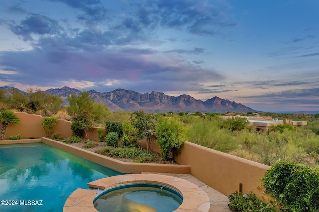 pool at dusk featuring an in ground hot tub and a mountain view