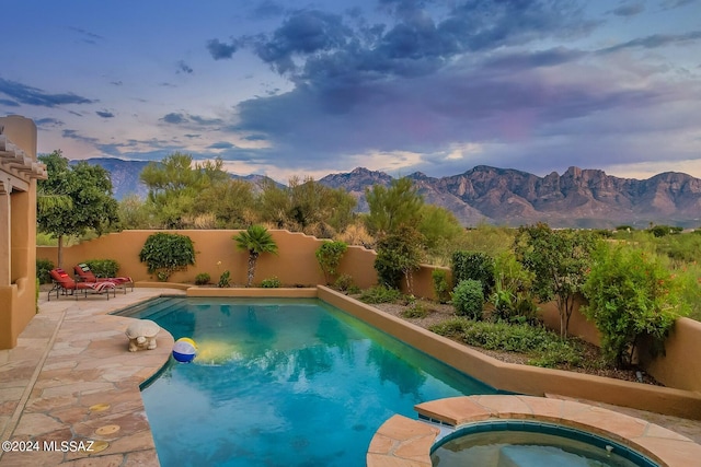 pool at dusk featuring an in ground hot tub, a mountain view, and a patio