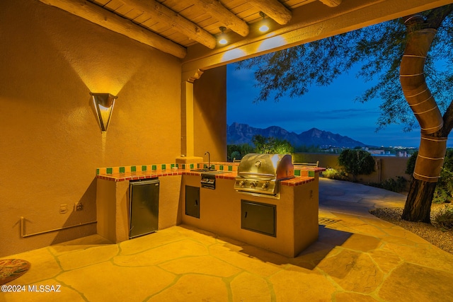 patio terrace at dusk with an outdoor kitchen, a mountain view, sink, and grilling area