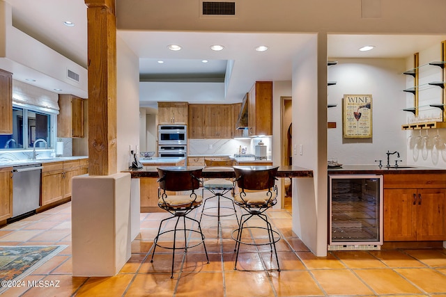 kitchen featuring light tile patterned flooring, a kitchen breakfast bar, wine cooler, decorative backsplash, and appliances with stainless steel finishes