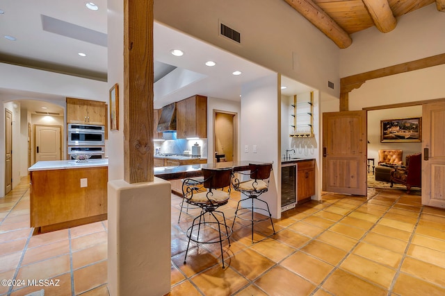 kitchen featuring wine cooler, light tile patterned floors, beam ceiling, kitchen peninsula, and decorative backsplash