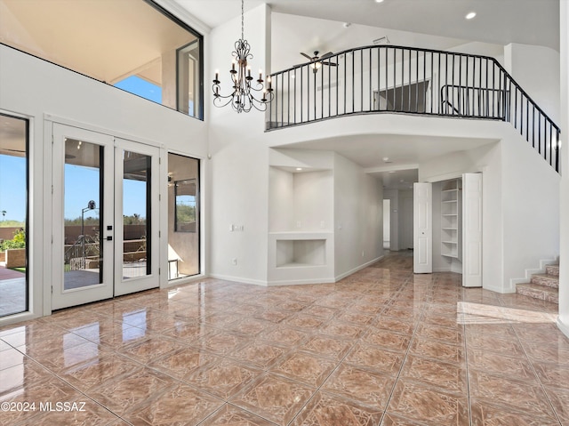 unfurnished living room featuring a chandelier, built in features, a towering ceiling, and french doors