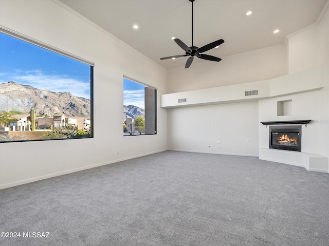 unfurnished living room with carpet, ceiling fan, crown molding, a mountain view, and a high ceiling