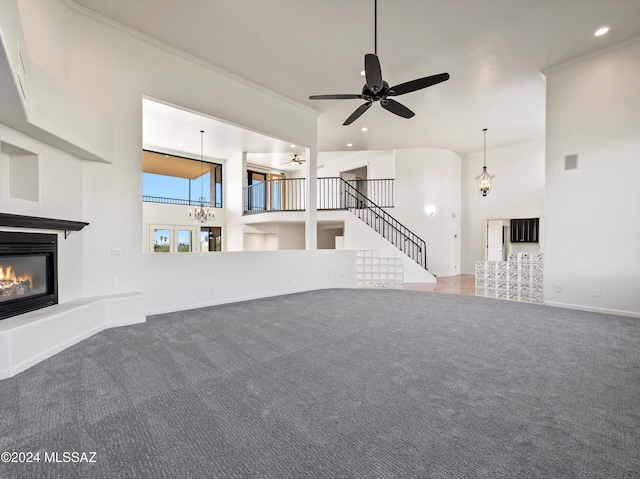 unfurnished living room featuring carpet, ceiling fan, a towering ceiling, and ornamental molding