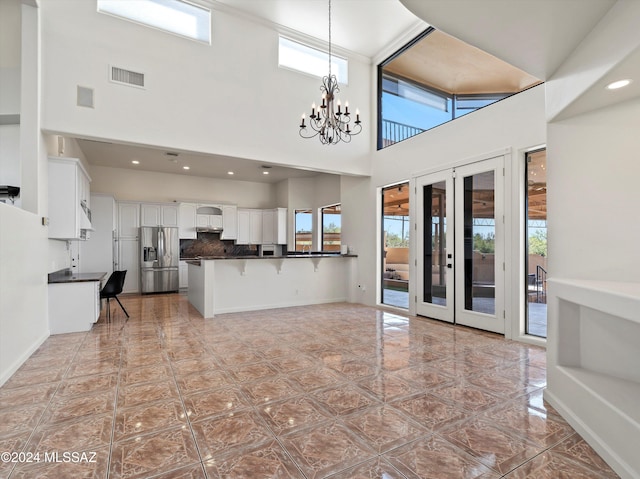 kitchen featuring stainless steel refrigerator with ice dispenser, kitchen peninsula, a towering ceiling, a kitchen bar, and white cabinets