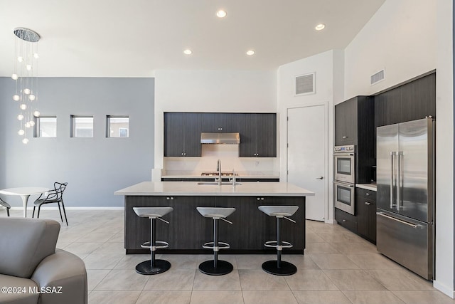 kitchen with a kitchen island with sink, light tile patterned floors, decorative light fixtures, a kitchen bar, and stainless steel appliances